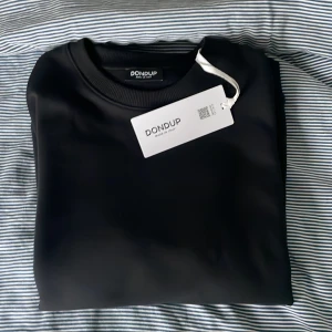 Svart sweatshirt från Dondup - Snygg svart sweatshirt från Dondup. Tröjan har en klassisk design med rund hals. Perfekt för en stilren outfit. Tröjan är helt oanvänd som ni ser så sitter till och med lappen kvar. Hör av er vid minsta fundering. Pris går även att diskuteras vid snabb affär 
