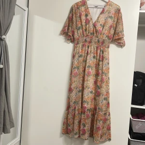 Blommig klänning från Amisu - Säljer en vacker blommig klänning från Amisu i storlek S. Klänningen har en v-ringad design med korta ärmar och ett elastiskt midjeband för en bekväm passform. Perfekt för sommarens alla tillfällen! 🌸