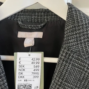 Oanvänd Svartvit rutig kavaj  - Snygg svartvit rutig kavaj från H&M. Den har en klassisk design med långa ärmar och två fickor framtill. Perfekt för en stilren look.