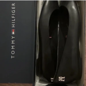 Svarta ballerinaskor från Tommy Hilfiger - Eleganta svarta ballerinaskor från Tommy Hilfiger med spetsig tå och en diskret logodetalj framtill. Köpte dem för ett jobb men har endast använt dem tre gånger inomhus, så de är i princip i nyskick. Nypris: 1200 kr.