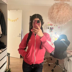 Rosa Adidas jacka med dragkedja - Säljer en snygg rosa Adidas jacka med dragkedja och vita detaljer eftersom den inte kommer till användning. Adidas-loggan syns både fram och bak.