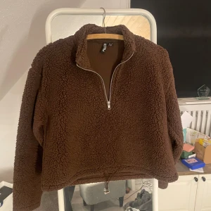 Brun fleece tröja från Pieces - Mysig brun fleece tröja från Pieces med dragkedja framtill. Perfekt för kyliga dagar med sin varma och mjuka känsla. Tröjan har en justerbar dragsko i nederkanten för en anpassad passform.