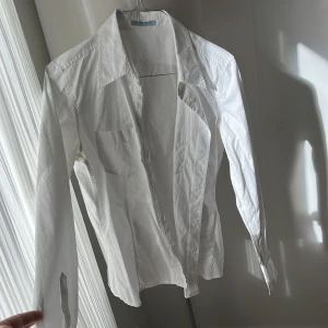 Vit skjorta från Strenesse - Snygg vit skjorta från Strenesse med klassisk krage och långa ärmar. Skjortan har knappar framtill och vid ärmsluten, vilket ger en stilren look. Perfekt för en chic och tidlös stil.