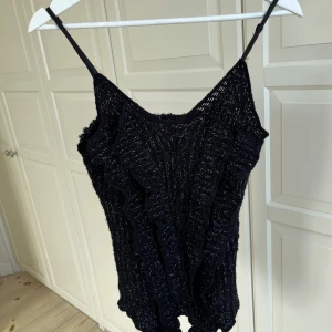 Svart stickad linnetopp från Sophyline - Snygg svart stickad linnetopp från Sophyline med volangdetaljer. Perfekt för en stilren look med smala axelband och en luftig design.