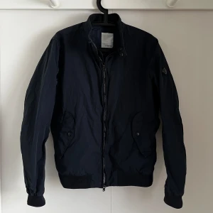 Svart jacka från J.Lindeberg - Riktigt fett marinblå jacka från J.Lindeberg i storlek M. Perfekt för våren säljs då jag har en liknande jacka redan så den kommer inte till användning. Nypris ca 2399 kr