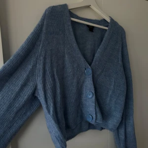 Blå kofta - Mysig blå croppad kofta från Lindex med stora knappar framtill. Den har en v-ringad design och är perfekt för kyligare dagar. Koftan är stickad och har en avslappnad passform. Använd 1-3 gånger 🩵🫐❄️