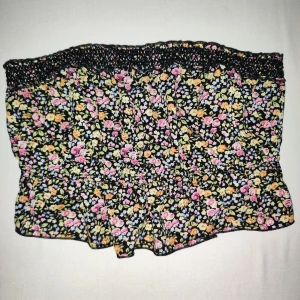 Blommig tubtopp - Snygga tubtopp från Bik Bok i storlek M. Den har ett färgglatt blommönster i rosa, gul och lila på en svart bakgrund. Toppen har ett elastisk band för extra komfort och en luftig passform.