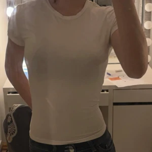 Vit t-shirt från Gina Tricot - Säljer en klassisk vit t-shirt från Gina Tricot. Den har en rund hals och korta ärmar, perfekt för en enkel och stilren look.