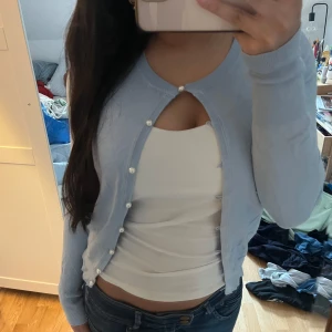 Ljusblå kofta med pärlknappar - Söt ljusblå kofta med långa ärmar och pärlknappar framtill. 