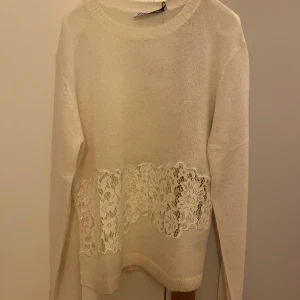 Vit stickad tröja med spetsdetalj - Säljer en stilren vit stickad tröja från Zara med en fin spetsdetalj runt midjan. Tröjan har långa ärmar och en rund halsringning. 