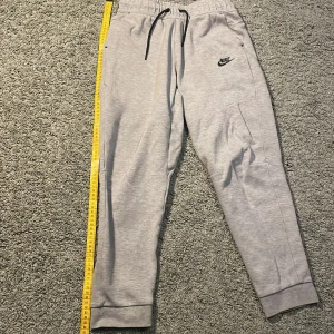 Grå mjukisbyxor från Nike - Säljer ett par grå mjukisbyxor från Nike i storlek XL. Byxorna har en elastisk midja med snörning och en liten Nike-logga på benet. Perfekta för en avslappnad stil.