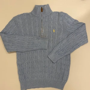 kabelstickad Ralph Lauren träja - Säljer en stilren ljusblå kabelstickad tröja från Polo Ralph Lauren i 100% tussah silke. Tröjan har en halv dragkedja och det ikoniska gula broderade logotypen på bröstet. Perfekt för kyliga dagar. Den är i bra skick förutom att den har två fläckar som ni ser på bild 5 men går nog bort i tvätten med rätt tvätt medel, skriv vid minsta fråga eller fundering🔥👍