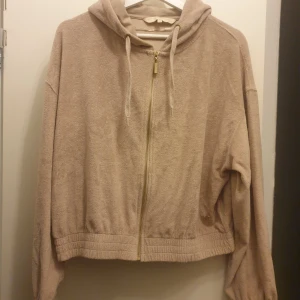 Pernilla Wahlgren mys tröja - Säljer en beige mys hoodie med dragkedja och huva. Den har långa ärmar och en avslappnad passform. Perfekt för en bekväm och stilren look. Jätte mjukt frotté tyg. 