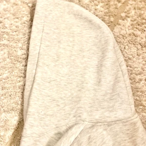 Grå hoodie från Adidas - Säljer en stilren grå hoodie från Adidas med den klassiska loggan i blått på bröstet. Tröjan har en känguruficka och långa ärmar med ribbade muddar. Perfekt för en avslappnad stil.