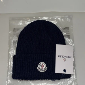 Mörkblå stickad mössa - Snygg mörkblå stickad mössa med broderad logotyp framtill. Perfekt för kyliga dagar och ger en stilren look.