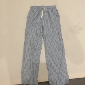 Randiga byxor från Lindex - Säljer ett par bekväma och stilrena randiga byxor från Lindex. De är ljusblå med vita och svarta ränder och har en elastisk midja med snörning för extra komfort. Perfekta för en avslappnad stil.