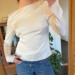 Vit långärmad topp med öppen rygg NAKD - Elegant vit topp med långa ärmar och en stilren öppen rygg. Perfekt för en chic och modern look.