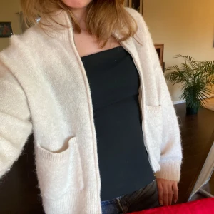Beige stickad kofta Second Female med dragkedja/zip - Mysig beige stickad kofta med långa ärmar och praktiska fickor framtill. Perfekt för kyligare dagar och ger en avslappnad look. Passar bra över en enkel topp eller t-shirt. Knappt använd!
