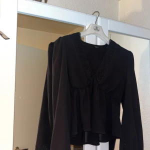 Svart blus med spetsdetaljer - Elegant svart blus från Shein med v-ringning och spetsdetaljer längs halsringningen. Den är ganska tunn men bekväm, den har använts ofta men inga skador