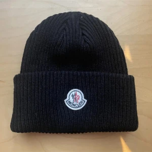 Svart mössa från Moncler - Snygg svart mössa från Moncler med  logga framtill. Perfekt för kyliga dagar och ger en stilren look.
