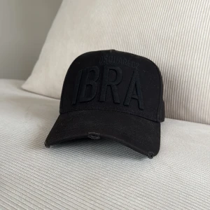 Svart keps från Dsquared2 - Snygg svart keps från Dsquared2 med texten 'IBRA' broderad framtill. Kepsen har en justerbar rem baktill för perfekt passform. En del av Zlatans kollektion, nypris 1699 kr