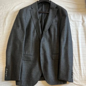 Grå kavaj och byxor från Hugo boss  - Snygg grå kostym från Vitale Barberis Canonico i Super 120 ull. Kavajen har klassisk design med knappar på ärmarna och byxorna har en stilren passform. 