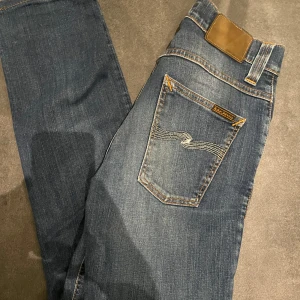 Nudie grim tim  - Säljer ett par snygga blå jeans från Nudie. Jeansen har en normal passform och är tillverkade i ekologisk bomull. Perfekta för en stilren look. 