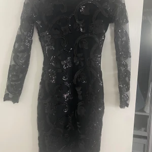 Svart glittrig klänning - Snygg svart klänning med glittriga detaljer och långärmad design. Den går att stänga hela vägen men tyvärr tight på mig därför ser det ut som att den är öppen,  klänningen har en tight passform som framhäver figuren. Perfekt för en festkväll!