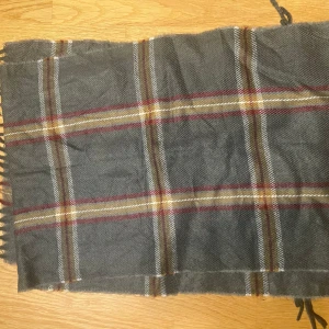 Grå Burberry halsduk - Snygg grå burberry halsduk med klassiskt rutmönster i rött, beige och vitt. Tillverkad i mjukt material med fransar i ändarna. Perfekt för att hålla sig varm och stilren under kyliga dagar.