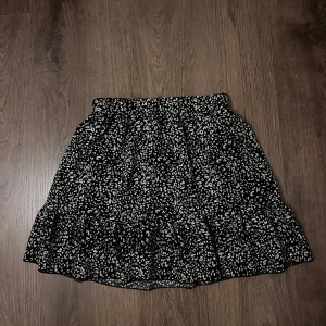 Svart och vit mönstrad kjol - Snygg svart kjol med vitt mönster och volangdetaljer. Perfekt för att ge en trendig touch till din outfit. Kjolen har en bekväm passform och är lätt att matcha med olika toppar.