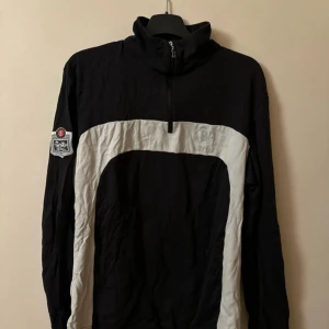 Svart och vit jacka från Bogner - Snygg svart och vit jacka från Bogner med dragkedja och hög krage. Jackan har en cool patch på ärmen och en kontrasterande vit panel framtill. Perfekt för en sportig look.