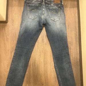 Blå jeans från Replay - Snygga blå jeans från Replay med klassisk femficksdesign och diskreta slitningar. Jeansen har en normal passform och är perfekta för en avslappnad stil. Märkeslogga på bakfickan och knappgylf framtill.