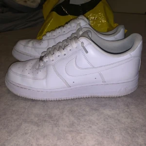 Vita Nike Air Force sneakers (Använd ett par gånger) - Säljer ett par klassiska vita Nike Air Force sneakers. Skorna har en stilren design med snörning och perforerade detaljer på ovansidan för ventilation. Perfekta för en avslappnad och trendig look. Dem är helt nya typ köpte från mos knappt använda.