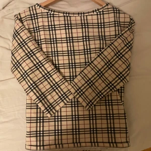 Rutig topp från Burberry - Säljer en stilren rutig topp från Burberry. Toppen har trekvartsärmar och en klassisk rund halsringning. Perfekt för en elegant och tidlös look.