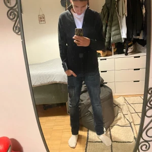 Svart ribbad kofta från indicode - Snygg svart kofta med dragkedja framtill. Den har en ribbad struktur och långa ärmar, perfekt för en stilren look. Passar bra till både jeans och chinos.