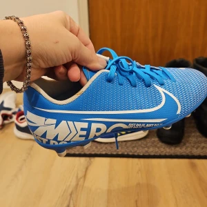 Blå fotbollsskor från Nike - Snygga blå fotbollsskor från Nike med vit logga och snörning. Perfekta för fotbollsplanen med sin stilrena design och bekväma passform.