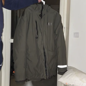 Grön Helly Hansen, Tromsoe Vinterjacka. - Tromsoe är en bekväm vinterjacka för herr från Helly Hansen. Nypris 3500 | Denna jacka är vadderad med High Loft™-polyester för att hålla dig varm även i minusgrader Jackan är tillverkad i ripstopmaterial med bra väderskydd och god ventilation tack vare de tejpade sömmarna och den PFC-fria vattenavvisande behandlingen. Jackan har hög krage och avtagbar, justerbar huva som skyddar extra mot kalla vindar och fallande snö Material 100% polyamid Foder 100% polyamid Fyllning 100% polyester (Byte går)