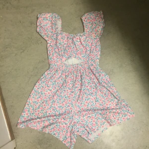 Blommig sommar-jumpsuit✨ - Charmig blommig jumpsuit i rosa och blått med en söt cut-out detalj i midjan. Jumpsuiten har korta ärmar och en luftig passform, perfekt för varma sommardagar☀️ Säljer eftersom att jag inte använder längre💕 Ser dock ut som en klänning men har inte några defekter alls!😋