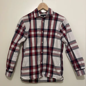 Skjorta från Tommy Hilfiger - Snygg rutig skjorta från Tommy Hilfiger i rött, vitt och blått. Skjortan har långa ärmar och klassiska knappar framtill. Perfekt för en stilren look.