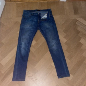 Blå jeansbyxor - Snygga blå jeansbyxor med en klassisk femficksdesign och en läderpatch på baksidan. De har en dragkedja och knapp framtill. Perfekta för en avslappnad stil.