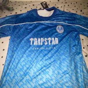 Trapstar fotbollströja - Snygg blå fotbollströja från Trapstar med korta ärmar och ett coolt mönster. Tröjan har vit text och nummer 22 på ryggen. Perfekt för dig som vill sticka ut på planen eller gatan.