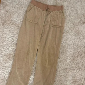 Beige mjukisbyxor från Juicy Couture - Säljer ett par supermjuka beige mjukisbyxor från Juicy Couture. Fickor både fram och bak. Liten defekt på ena benet längst ner, se bild 3💖