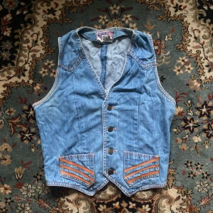 Blå jeansväst - En cool vintage jeansväst från Faded Glory med orangea detaljer på fickorna. 70-talet