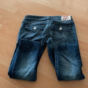 Blå jeans från True Religion - Snygga blå jeans från True Religion med skinny passform. De har en klassisk femficksdesign och dekorativa sömmar på bakfickorna. Perfekta för en stilren look. Säljer dessa då de är för små för mig. Använt 1 gång.