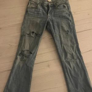 Blå jeans - Säljer ett par blå jeans. (Hålen har jag gjort själv) De har en klassisk femficksdesign och en bekväm passform. Utsvängda och lågmidjade