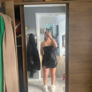 Perfekta nyårs klänningen  - Snygg svart axelbandslös klänning med glittriga paljetter och en liten slits. Endast använd 1 gång❣️ Perfekt för nyår eller nån annan glittrig kväll!💫