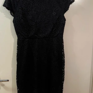 Svart spetsklänning från Vero Moda - Elegant svart klänning från only i storlek 38. Den har ett vackert spetsmönster och korta ärmar, perfekt för festliga tillfällen. Klänningen är figursydd och ger en smickrande passform. Ett måste för garderoben om du älskar klassisk stil!