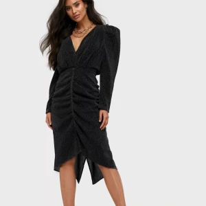 Adoore svart glittrig klänning  - Snygg svart klänning med glittrande tyg och puffärmar. Klänningen har en djup V-ringning framtill som kan framhävas ytterligare genom att lossa öglan och en öppen rygg. Den är figursydd och har en längd som når strax över knäna. Oanvänd.