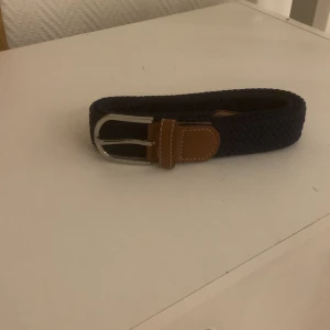 Flätar bälte - Blåt flätat bälte med läder detaljer. Fick bältet i present av min kompis som hade köpt den på john henric.  Bältet är 105cm långt. Skriv vid frågor eller flera bilder mvh ag