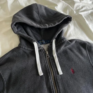 Polo Ralph Lauren Hoodie Huvtröja mörkgrå  - Använd och väl omhändertagen. Huvtröja från Polo Ralph Lauren, tillverkad i 100% bomull. Vinröd häst.                          Butikpris: 1 299kr